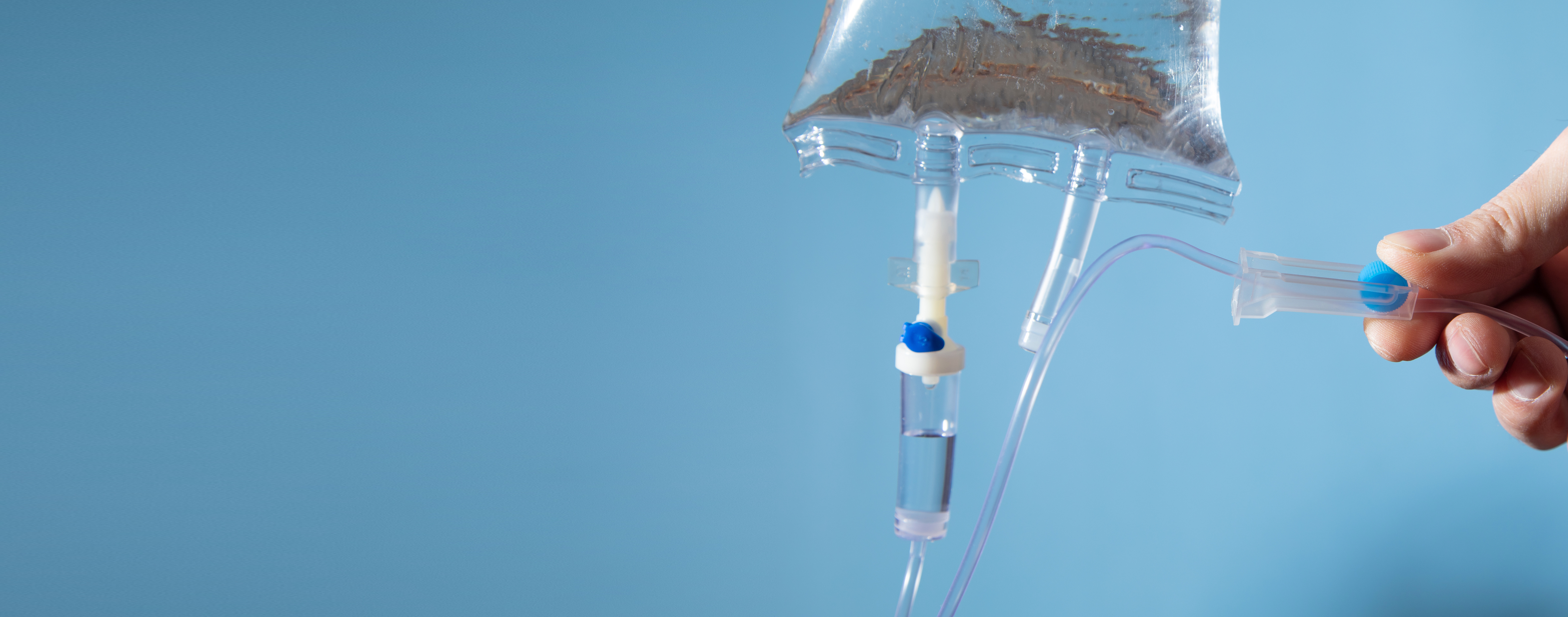 Hand holding an intravenous drip on the blue background.
