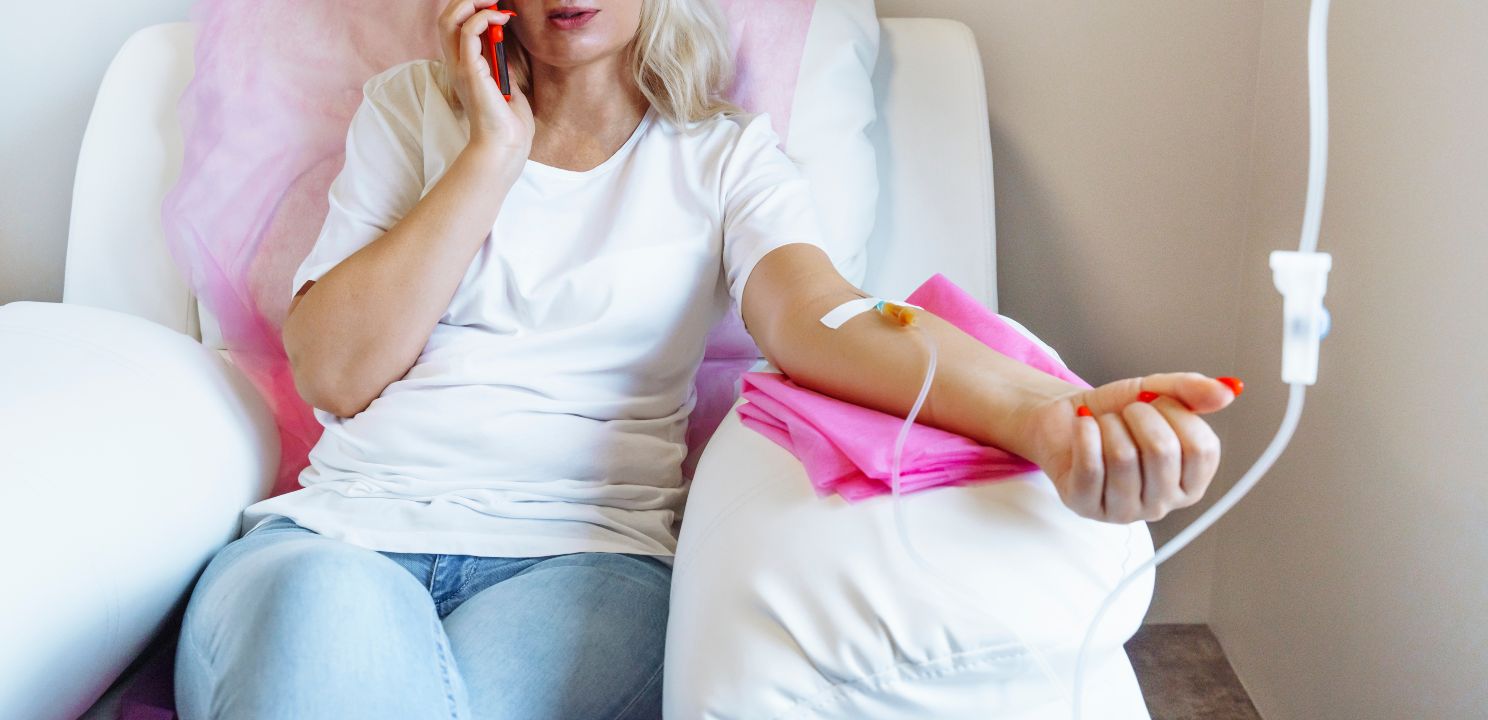 Woman in hospital talking at mobile phone while needle is in arm, Vitamin Therapy Iv Drip Infusion In Women Blood