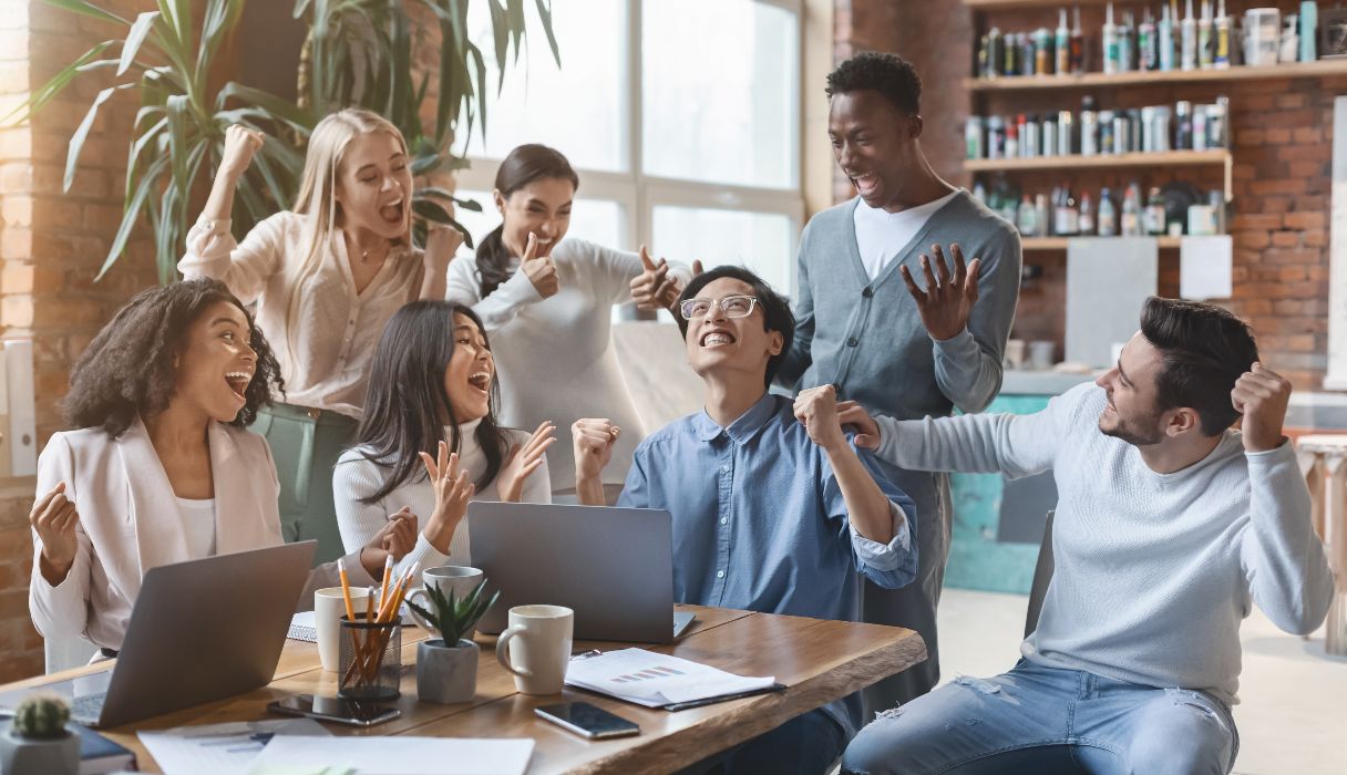 Happy young multiethnic team looking at laptop screen, celebrating success, at office, panorama 