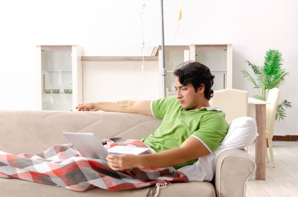 man in green shirt having iv while looking at the laptop at the living room. iv therapy for weight loss 