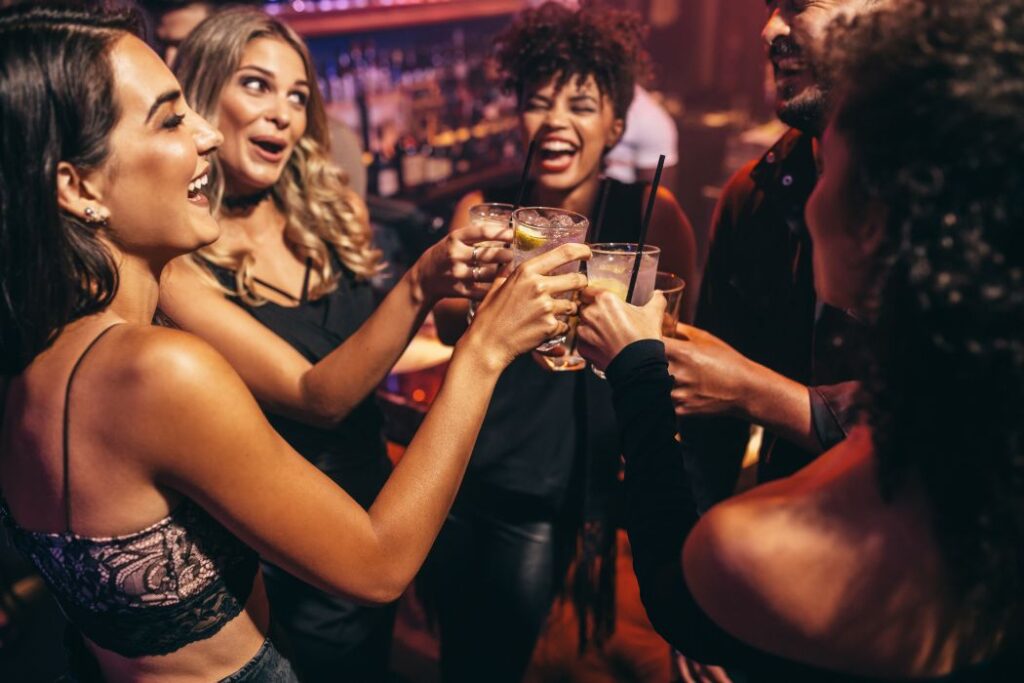 Group of friends partying in a nightclub and toasting drinks. Happy young people with cocktails at pub