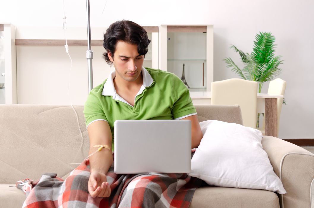 how long do iv fluids take. young man looking at his pc while in IV
