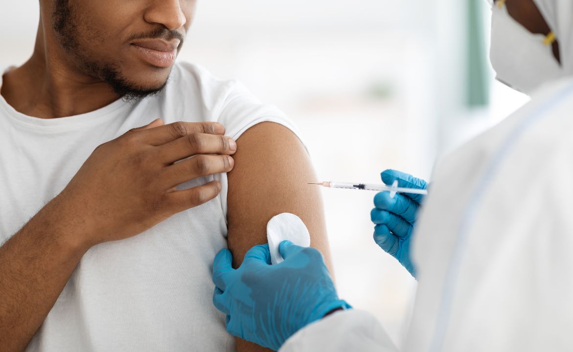 Vaccination and immunization concept. Cropped of young black man receiving vaccine shot during coronavirus pandemic. Closeup of doctor in PPE making injection in shoulder for male patient 