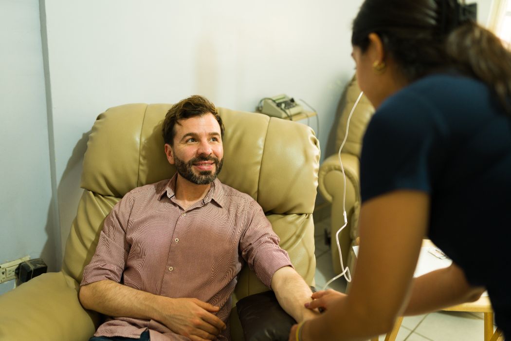 Attractive happy man talking to the nurse while getting alternative medicine and IV drip therapy for a myers vitamins cocktail. 