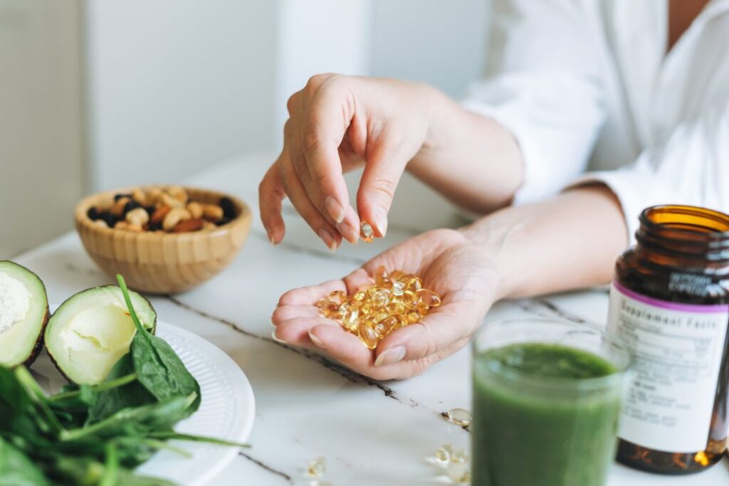 Woman doctor nutritionist hands in white shirt with omega 3, vitamin D capsules with green vegan food