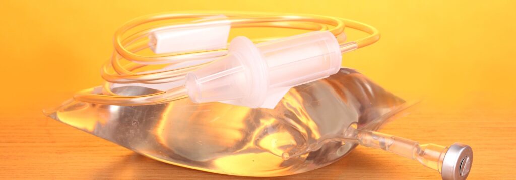 Bag of intravenous antibiotics and plastic infusion set on wooden table on yellow background