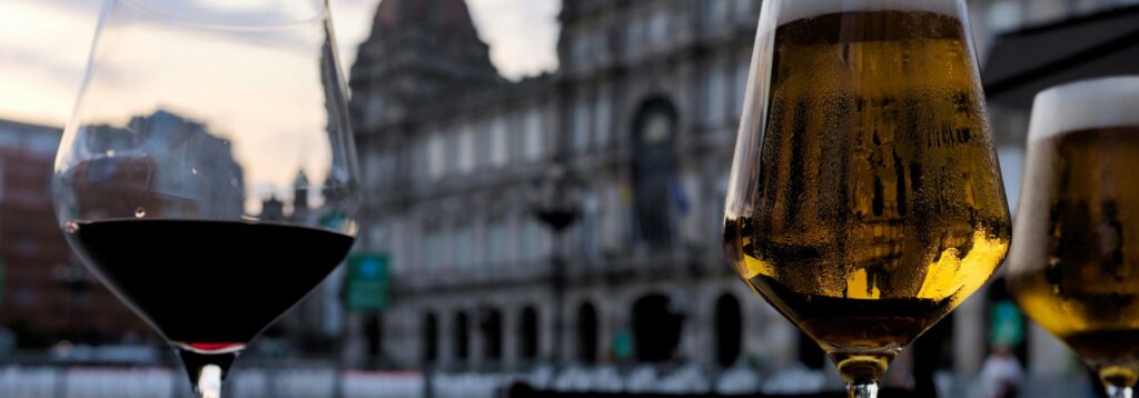 Two glasses of wine and beer sit on a table outside a building